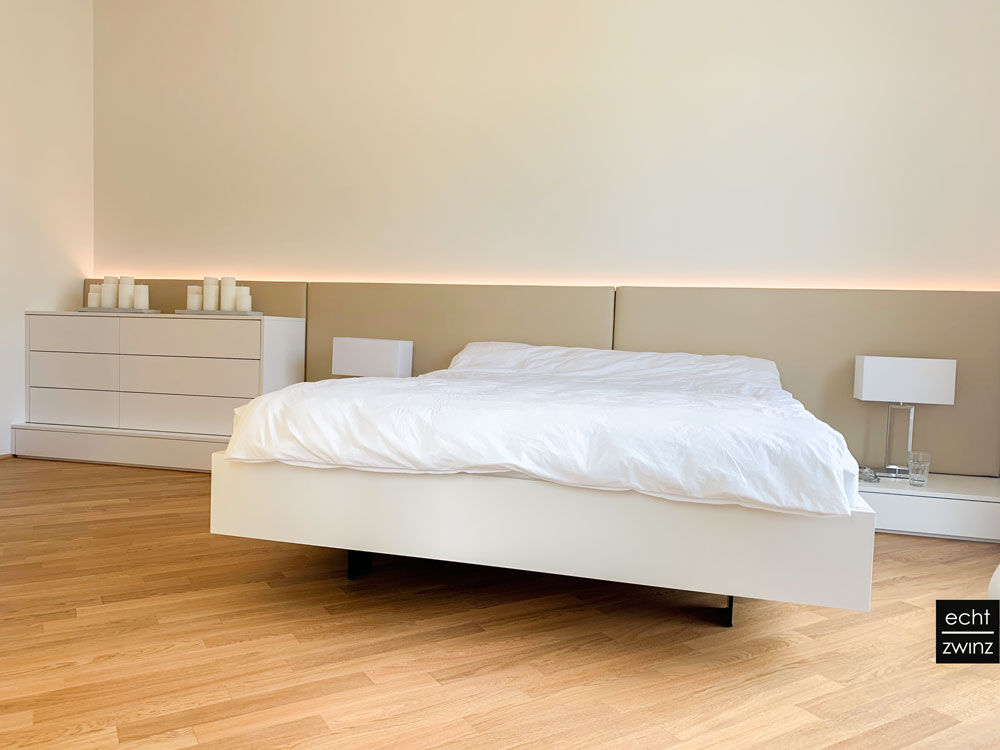 Weißes Schlafzimmer mit beigem Kunstleder-Polster als Rückwand und Nachttischarmaturen